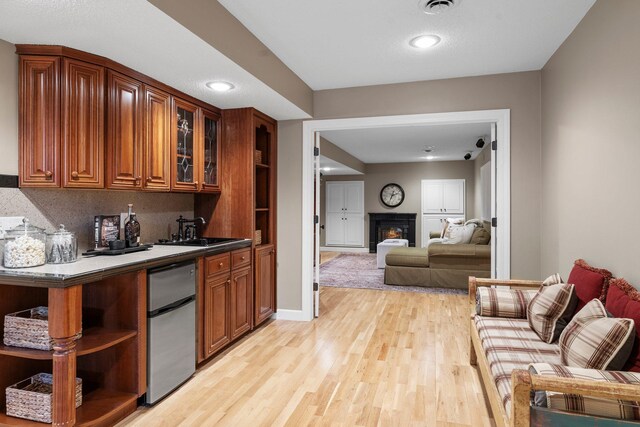 bar area with refrigerator, a sink, light wood-type flooring, a warm lit fireplace, and recessed lighting
