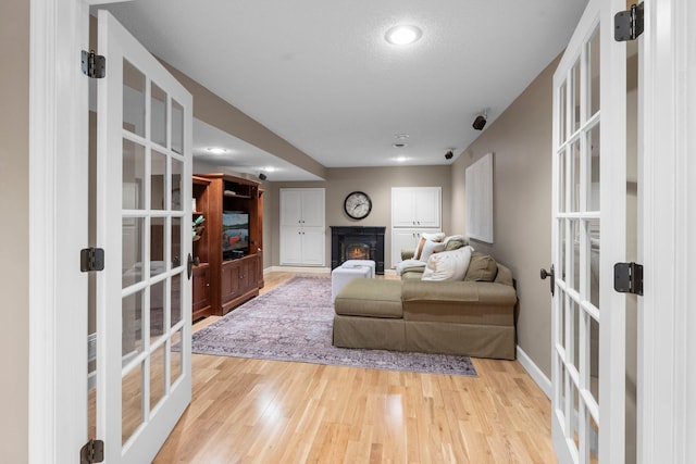 living room featuring french doors, a glass covered fireplace, light wood-type flooring, baseboards, and recessed lighting