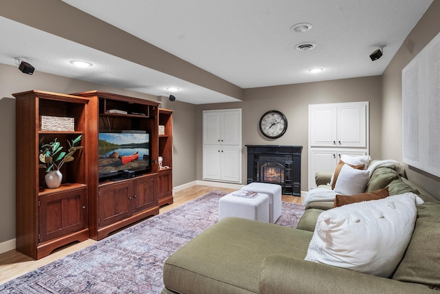 living room featuring light wood-type flooring, a warm lit fireplace, baseboards, and recessed lighting