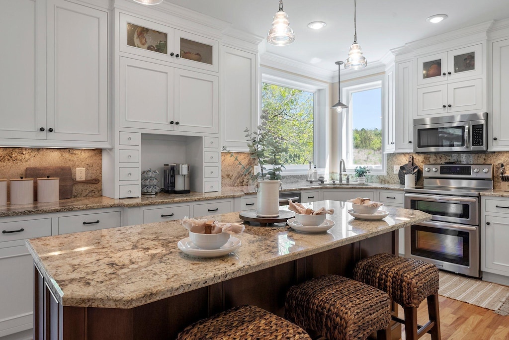 1400 Wildflower Ln, Chaska, MN 55318 - kitchen featuring appliances with stainless steel finishes, a sink, a breakfast bar area, hanging light fixtures, and white cabinetry