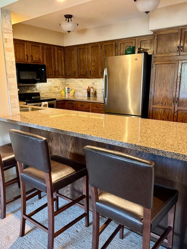 kitchen with a peninsula, stainless steel appliances, tasteful backsplash, and a kitchen breakfast bar