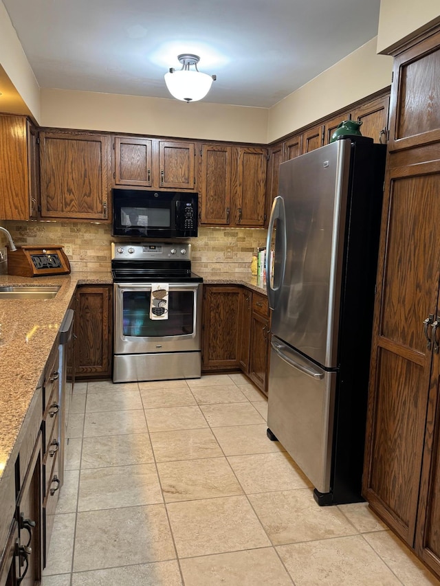 kitchen featuring light tile patterned floors, light stone counters, a sink, backsplash, and appliances with stainless steel finishes
