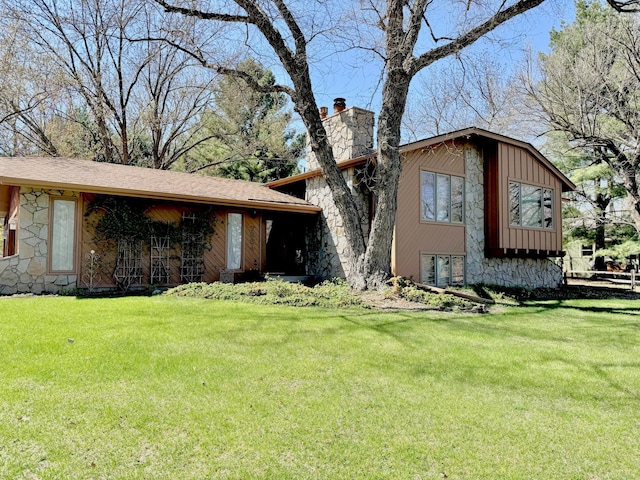 split level home with a chimney, stone siding, and a front lawn
