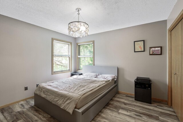 14250 Upper 54th St N, Oak Park Heights, MN 55082 - bedroom with wood finished floors, a chandelier, a textured ceiling, baseboards, and a closet