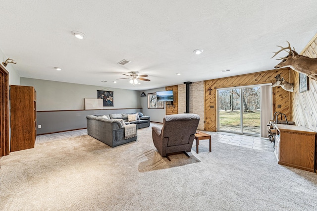 living area featuring light carpet, a wood stove, wood walls, and ceiling fan