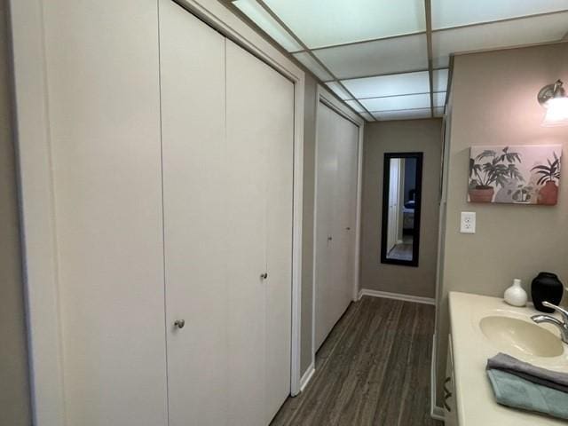 bathroom with baseboards, wood finished floors, vanity, and a paneled ceiling