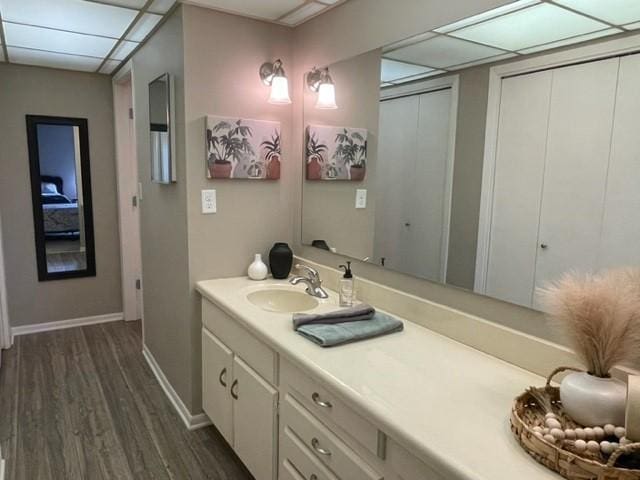 bathroom featuring baseboards, wood finished floors, vanity, and a paneled ceiling