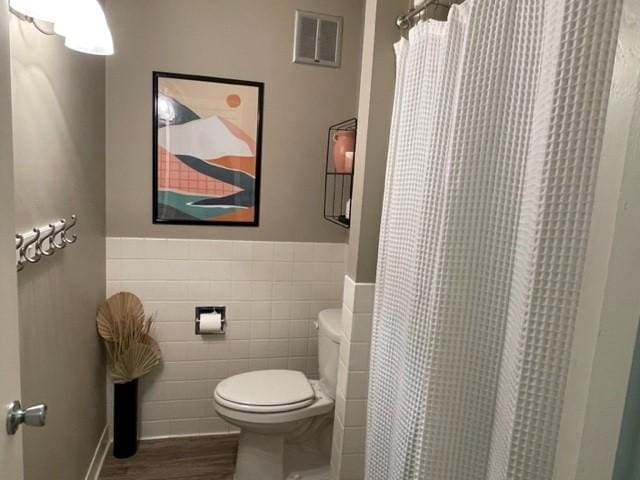 bathroom featuring toilet, tile walls, a wainscoted wall, wood finished floors, and visible vents