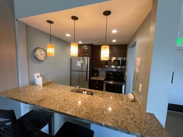 kitchen featuring a sink, a peninsula, light stone countertops, and appliances with stainless steel finishes