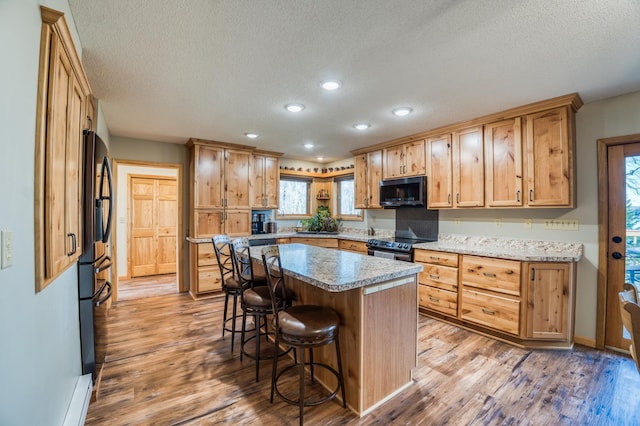 kitchen with a textured ceiling, light wood finished floors, a kitchen bar, electric range, and a kitchen island