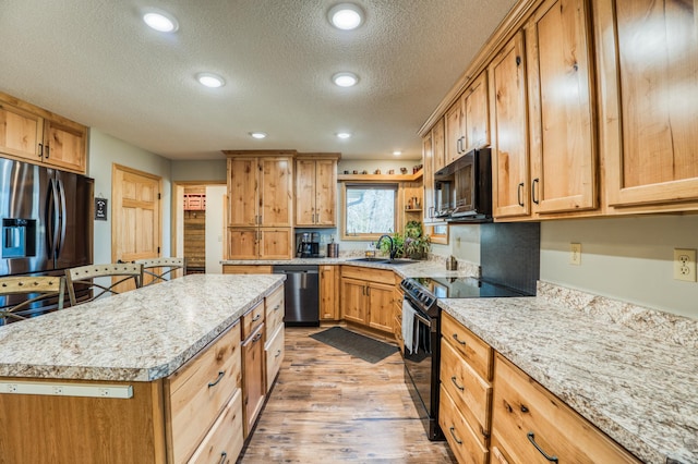 kitchen with a sink, a textured ceiling, light wood-type flooring, black appliances, and a kitchen island