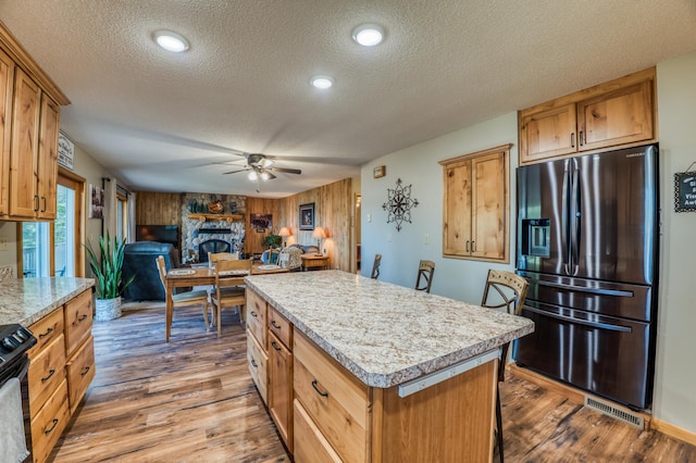 kitchen featuring a textured ceiling, stainless steel refrigerator with ice dispenser, ceiling fan, light countertops, and a center island