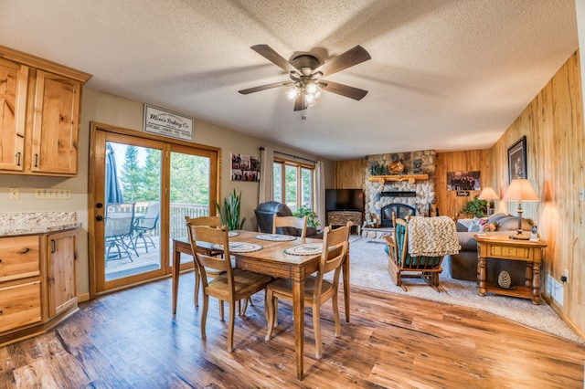 dining space featuring wooden walls, light wood-style flooring, ceiling fan, and a textured ceiling