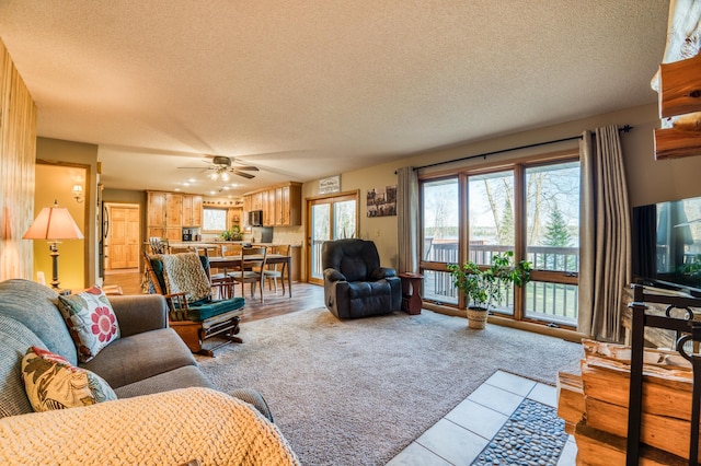 living area featuring light carpet, ceiling fan, a textured ceiling, and light tile patterned floors