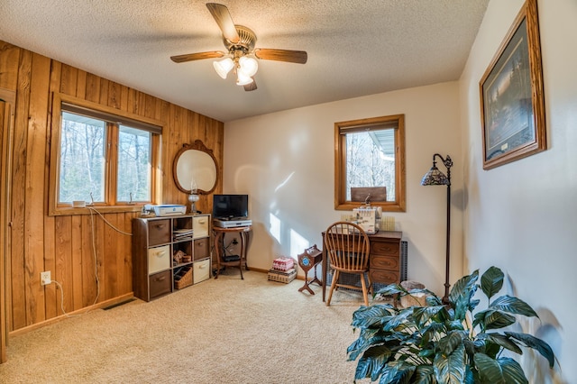 carpeted office with a textured ceiling, wood walls, baseboards, and a ceiling fan