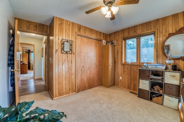 interior space with a textured ceiling, ceiling fan, wooden walls, carpet flooring, and baseboards