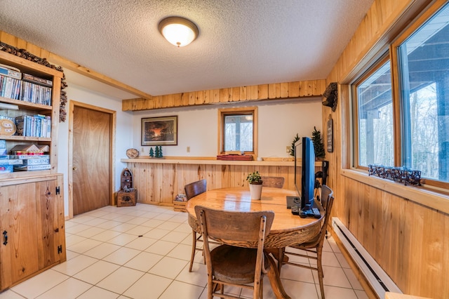 dining room with a textured ceiling, light tile patterned floors, baseboard heating, and wood walls
