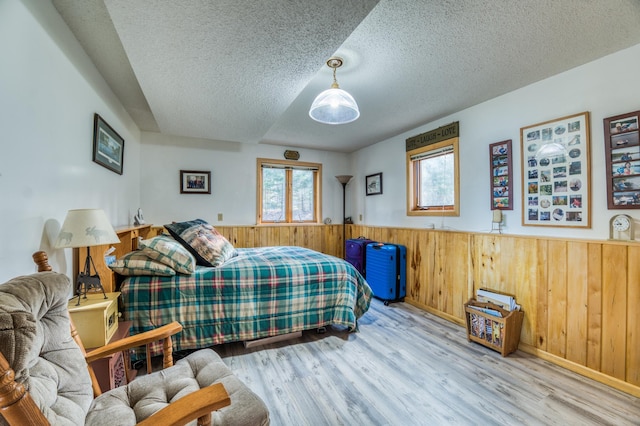 bedroom with a textured ceiling, wood walls, wood finished floors, and wainscoting
