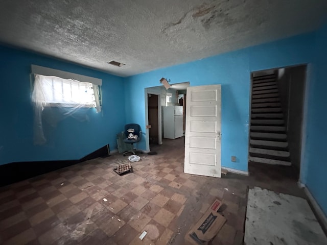 unfurnished bedroom featuring freestanding refrigerator, a textured ceiling, and visible vents