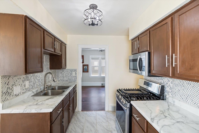 kitchen with appliances with stainless steel finishes, light marble finish floors, a sink, and backsplash
