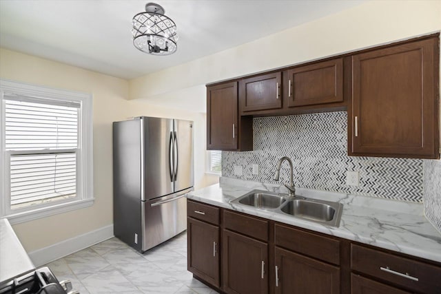 kitchen featuring freestanding refrigerator, a sink, light marble finish flooring, tasteful backsplash, and baseboards