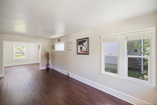 spare room featuring baseboards and dark wood-type flooring