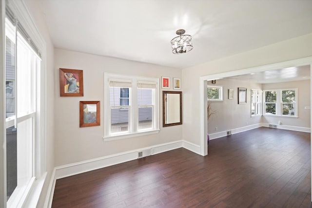 spare room with dark wood-style flooring, a chandelier, and baseboards
