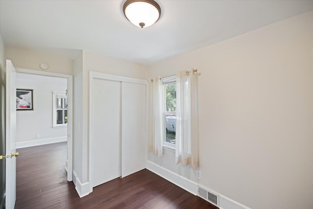 unfurnished bedroom featuring dark wood-type flooring, a closet, and baseboards