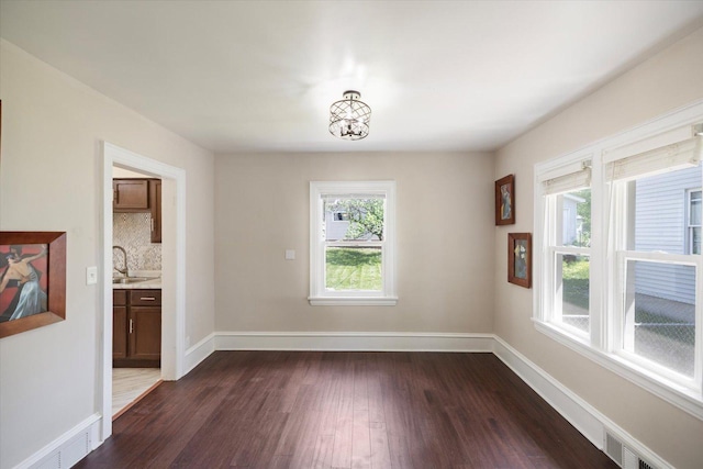 empty room featuring dark wood-style flooring, a sink, baseboards, and a chandelier