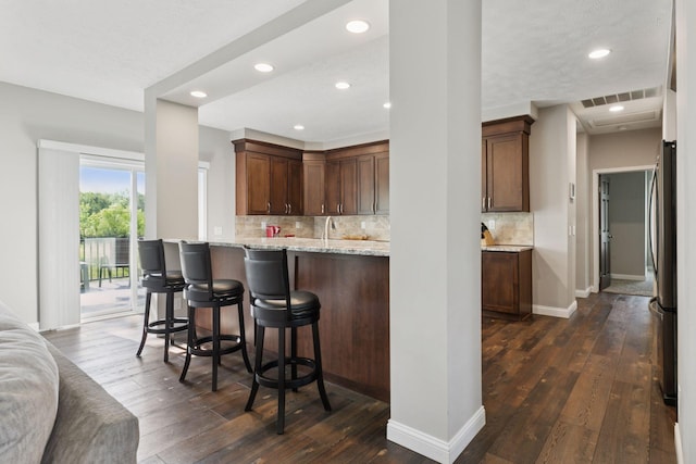 21212 Old Lake George Blvd NW, Oak Grove, MN 55303 - kitchen featuring dark wood-style flooring, freestanding refrigerator, backsplash, a kitchen breakfast bar, and light stone counters