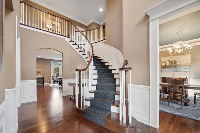 16302 Sohm Ct, Eden Prairie, MN 55347 - staircase featuring a wainscoted wall, a decorative wall, arched walkways, a chandelier, and hardwood / wood-style flooring