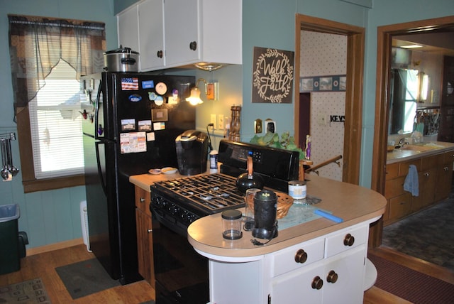 kitchen with black appliances, wood finished floors, light countertops, and white cabinetry