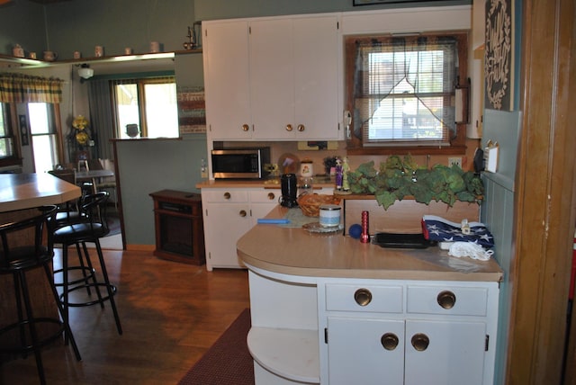 kitchen with stainless steel microwave, white cabinetry, wood finished floors, and light countertops