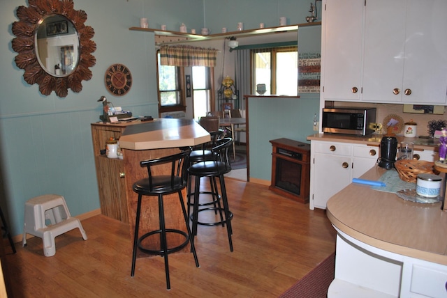 kitchen with stainless steel microwave, light wood-style flooring, white cabinets, light countertops, and wainscoting