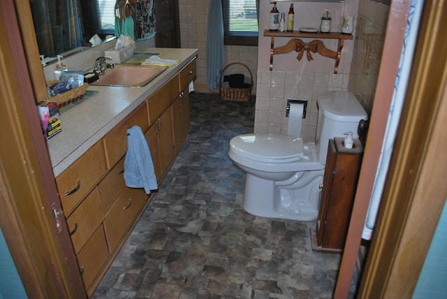 bathroom featuring tile walls, toilet, stone finish flooring, and vanity