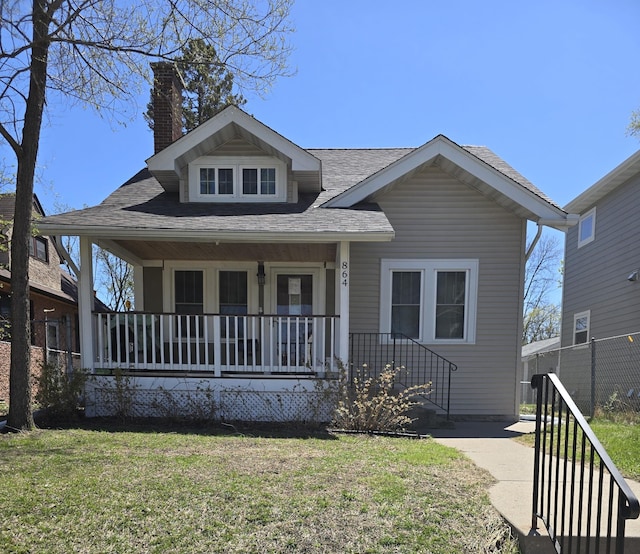 bungalow-style home featuring covered porch, roof with shingles, fence, a front lawn, and a chimney
