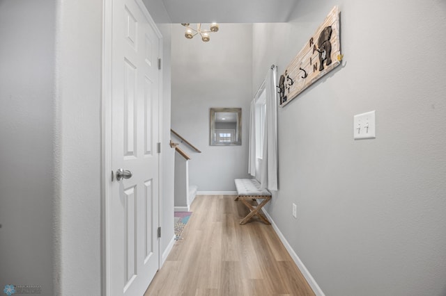 corridor featuring light wood-style flooring, a chandelier, baseboards, and stairway