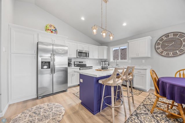kitchen featuring stainless steel appliances, vaulted ceiling, a sink, white cabinetry, and a center island