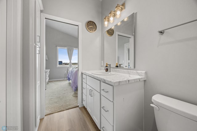 half bath featuring wood finished floors, toilet, vanity, and lofted ceiling