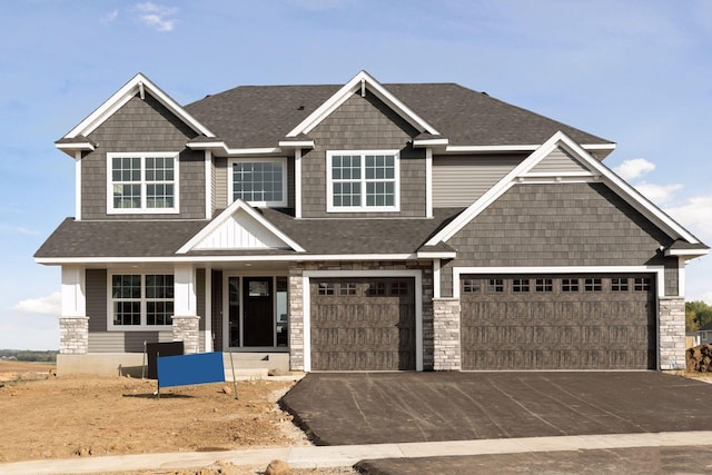 craftsman house with stone siding, a shingled roof, driveway, and an attached garage