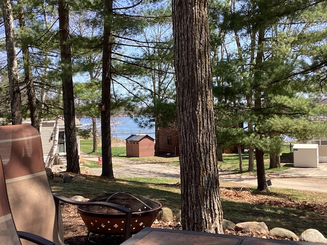 view of yard featuring a water view, a storage shed, a fire pit, and an outdoor structure