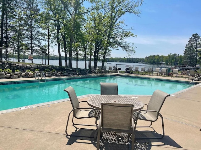 community pool with fence, a patio area, and a water view