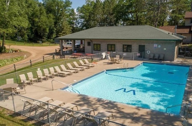 community pool featuring a patio area, fence, and view of wooded area