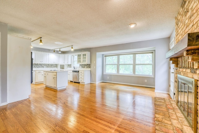 1900 Vernon Dr S, Minnetonka, MN 55305 - unfurnished living room with a stone fireplace, a textured ceiling, light wood-type flooring, track lighting, and baseboards