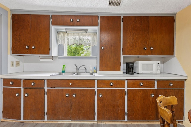 100 2nd St S, Delano, MN 55328 - kitchen featuring a sink, white microwave, light countertops, brown cabinetry, and a textured ceiling