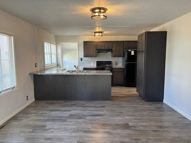 kitchen featuring under cabinet range hood, a peninsula, wood finished floors, and black appliances