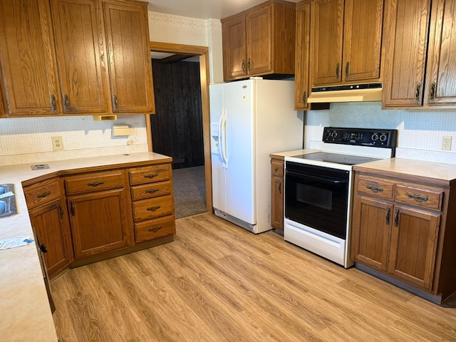 314 Burr Oak Dr, Albert Lea, MN 56007 - kitchen with electric range, under cabinet range hood, white fridge with ice dispenser, brown cabinets, and wallpapered walls