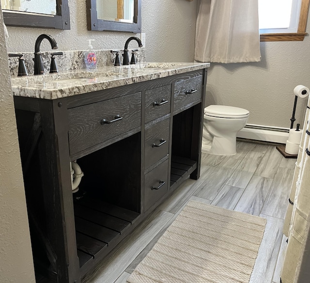 2250 18th Ave, Windom, MN 56101 - bathroom with a baseboard radiator, a textured wall, double vanity, and wood finished floors