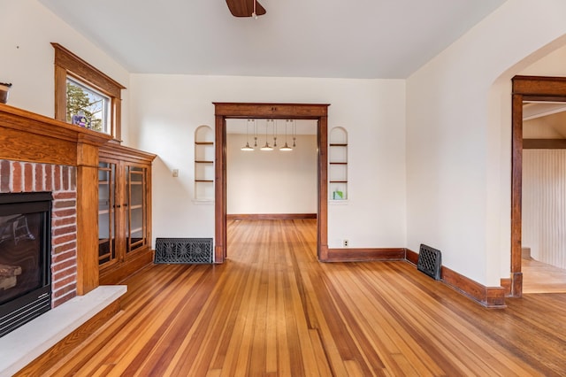 unfurnished living room featuring baseboards, a fireplace, hardwood / wood-style floors, and arched walkways