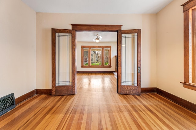 hall featuring visible vents, light wood-style flooring, and baseboards